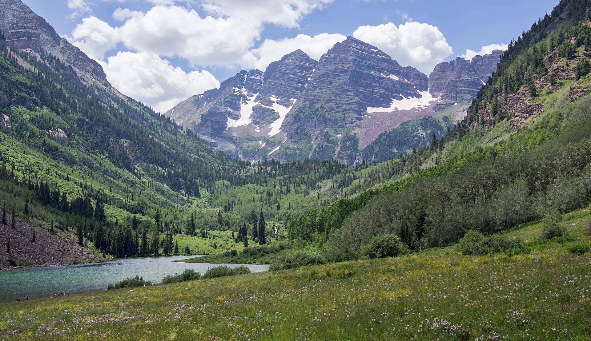 The Maroon Bells rising above a green valley and lake near Aspen, Colorado, on a sunny day